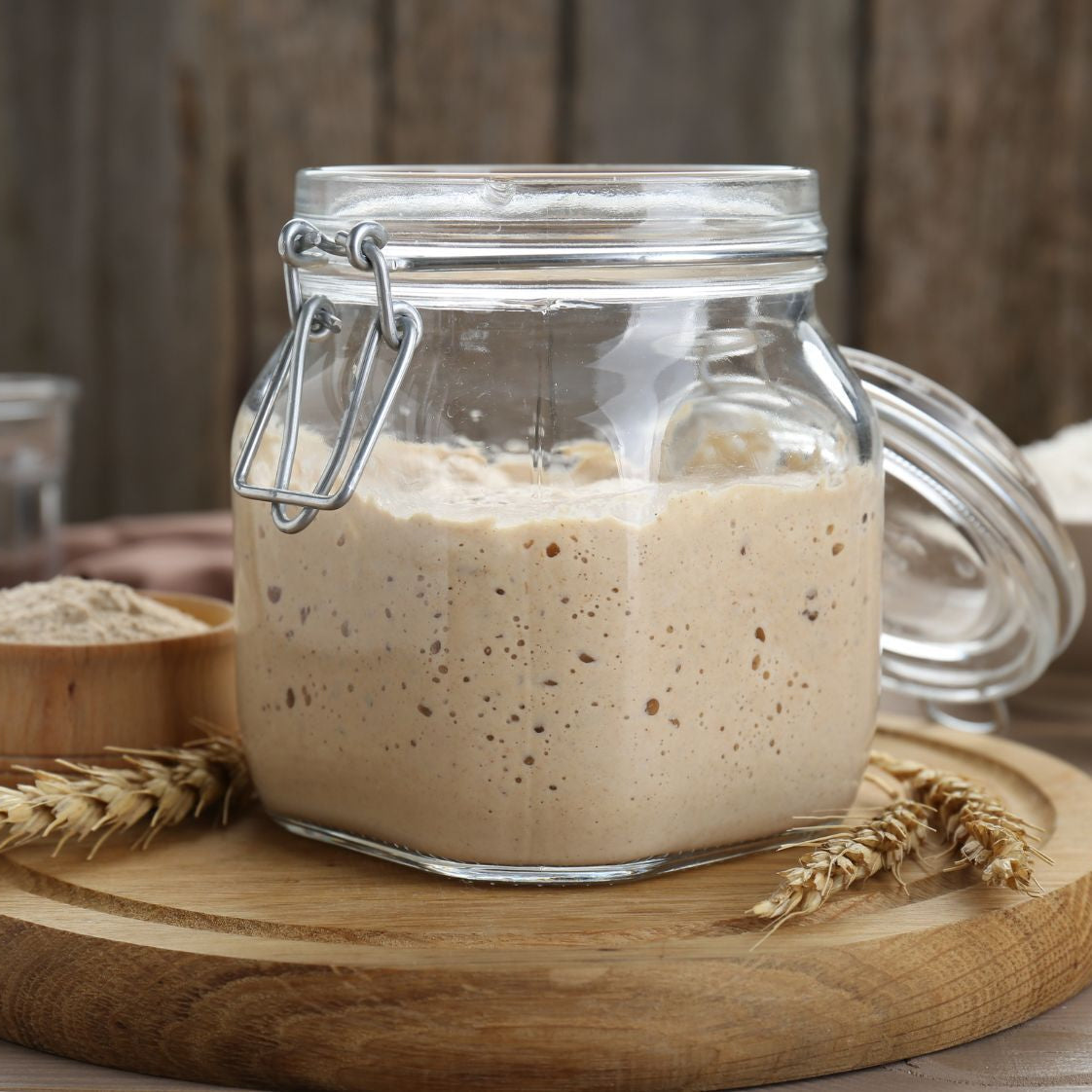 Glass jar with San Franciscian sourdough starter on a wooden board with a rustic background