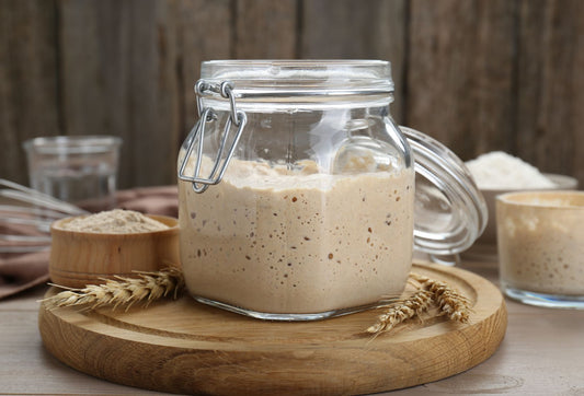 Glass jar with sourdough starter on a wooden board with a rustic background