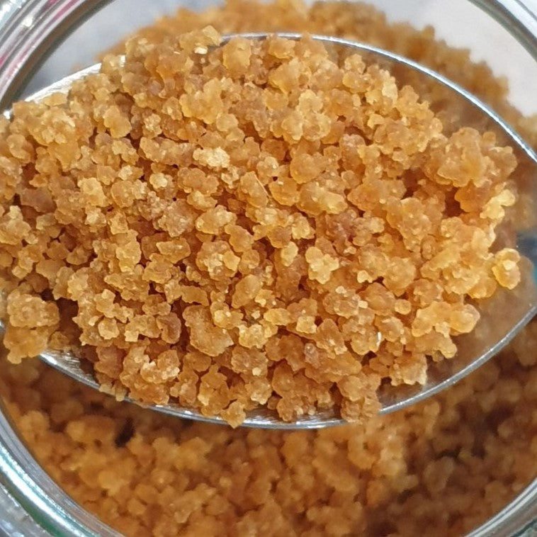 Dehydrated water kefir grains on a spoon, with a jar of dried kefir grains in the background.