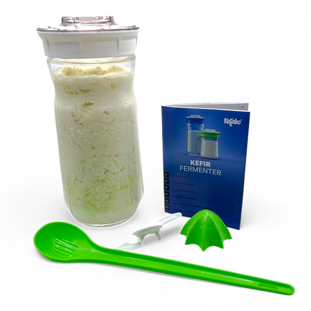 Large white Kefirko fermenter kit with milk kefir grains, a green spoon, and a blue manual on a white background