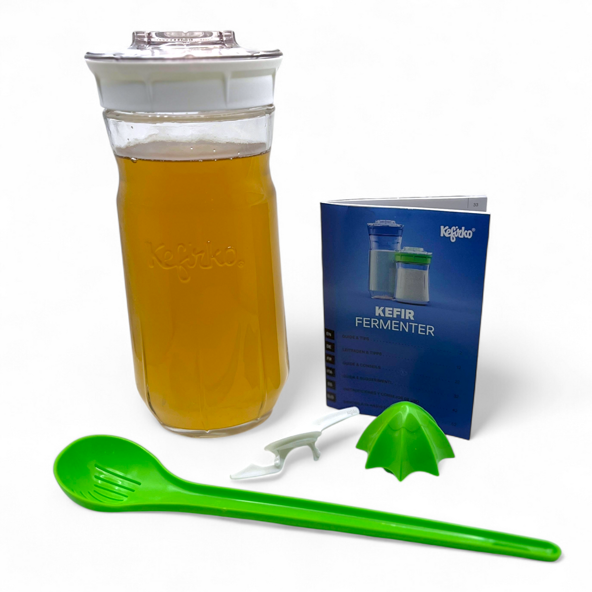 Large white Kefirko maker kit with water kefir grains, green spoon, and blue manual on a white background