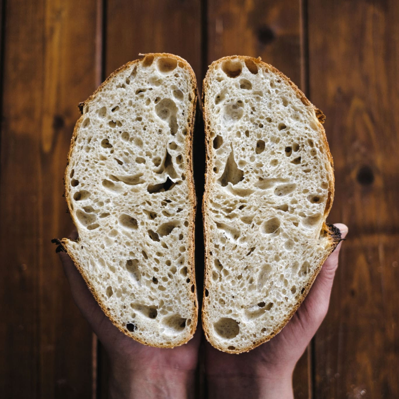 Hand holding a sliced loaf of homemade bread against a wooden background