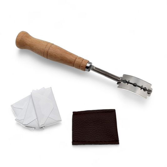 Wooden handled bread lame sitting next to spare blades in a white envelope and a brown leather cover