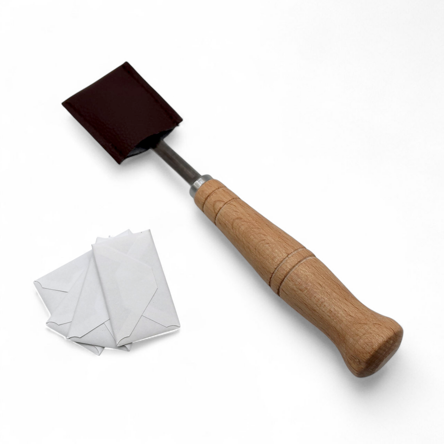 Bread lame with wooden handle sleeved by a brown leather cover, sitting next to white paper envelopes containing blades on white background