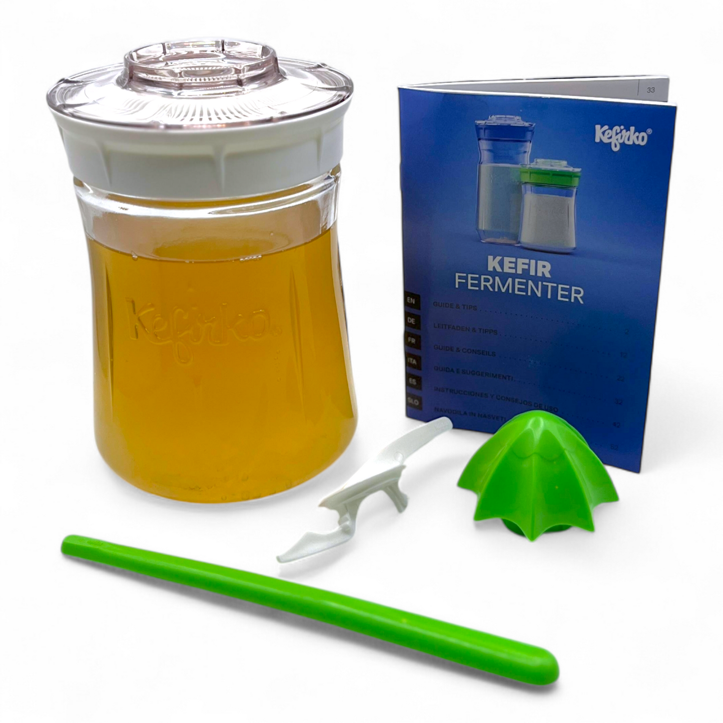 Small white Kefirko fermenter with water kefir, green tool, and blue manual on a white background