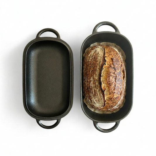 Loaf of freshly baked sourdough on baking paper sitting inside body of dutch oven with lid of dutch oven lying next to it. 
