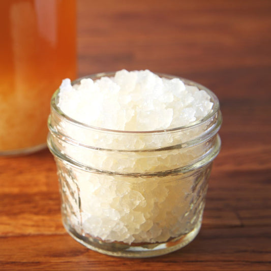 Glass jar filled with water kefir grains on wooden table with jar of water kefir in background. 